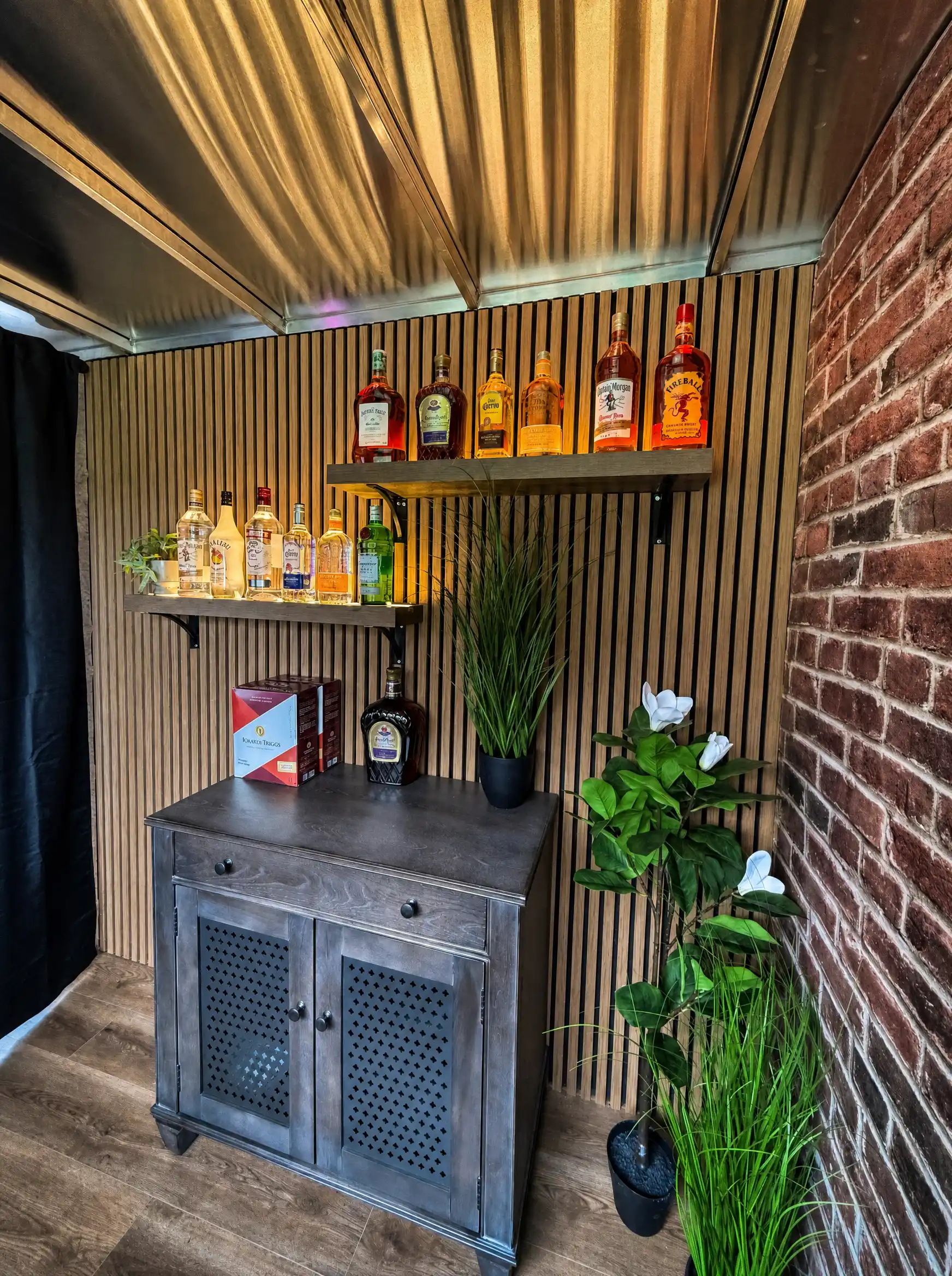A corner of the bar stocked with spirits and greenery under warm golden light.